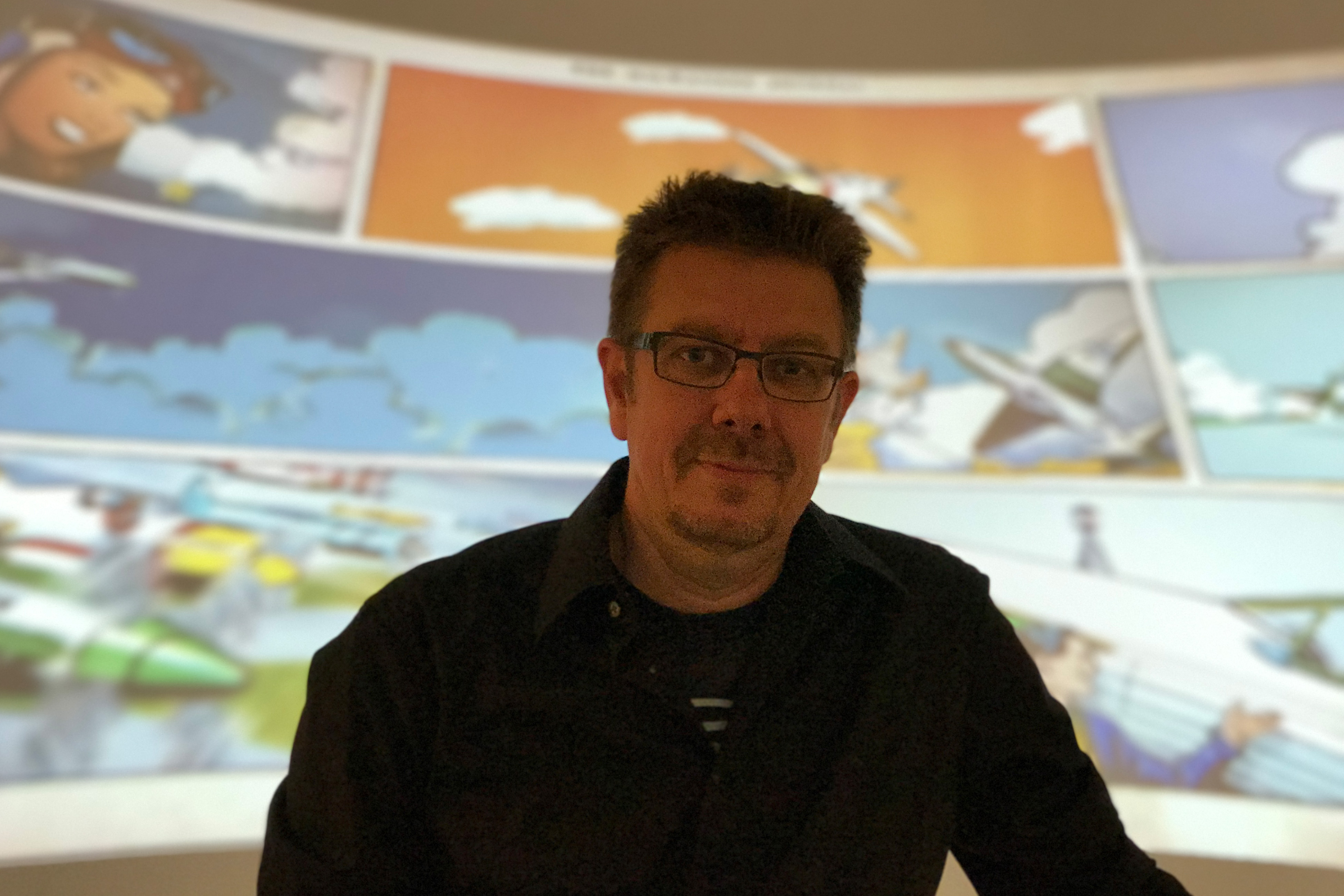 Alexander Braun posiert vor einem Comic-Film, der in der Ausstellung gezeigt wird